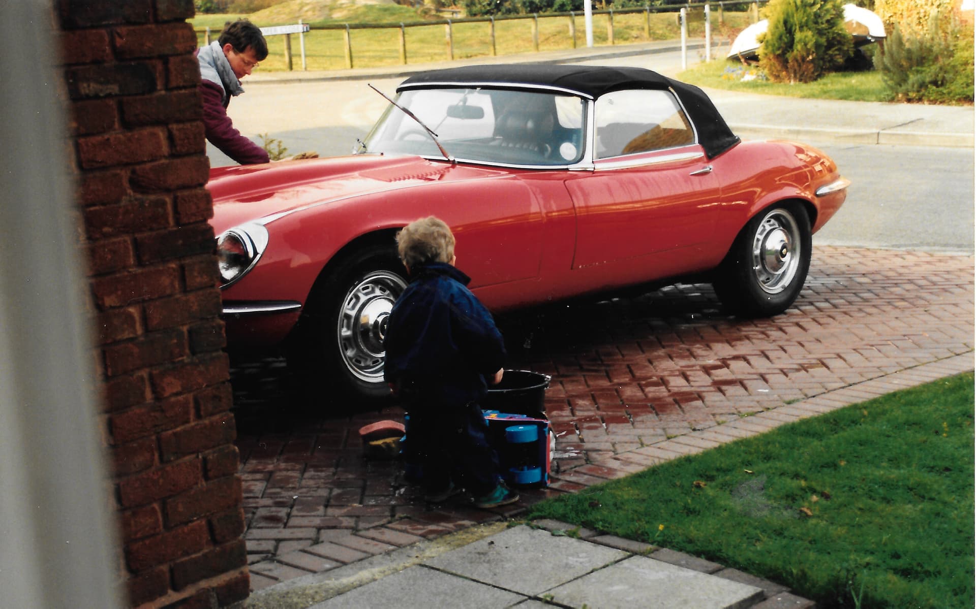 A father and son washing a classic Jaguar E-Type on the driveway